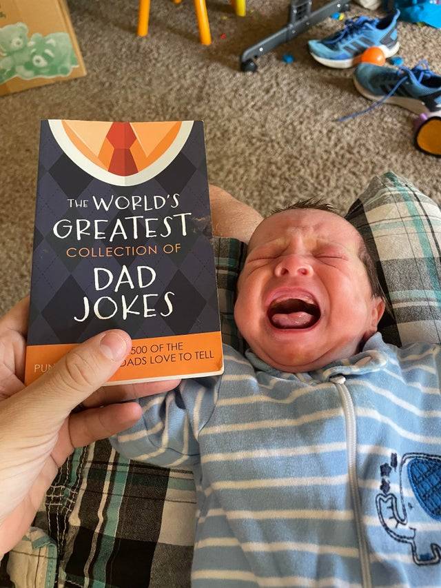 Baby crying and screaming while dad holds dad jokes book
