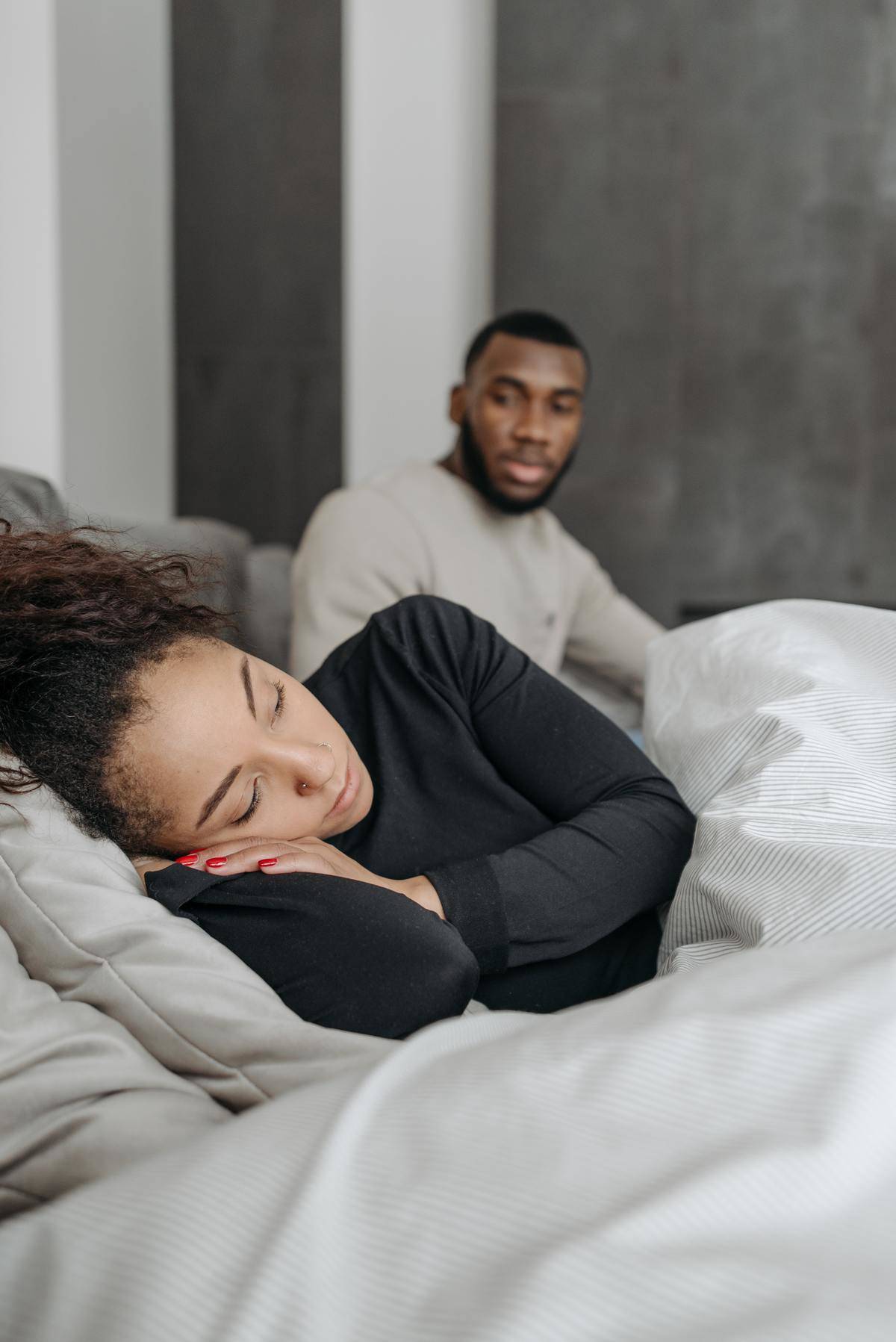 Man and woman in bed, woman facing away from man 