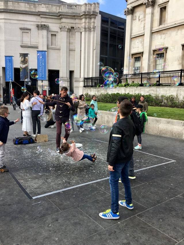 Group of people outside at a fountain and a child is about to fall on the ground.