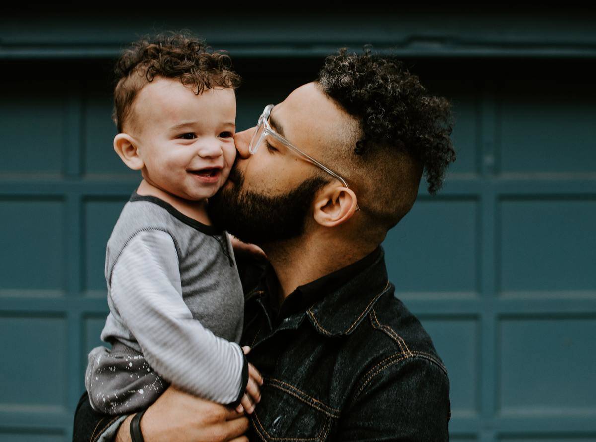 A father kisses his toddler-aged son on the cheek.