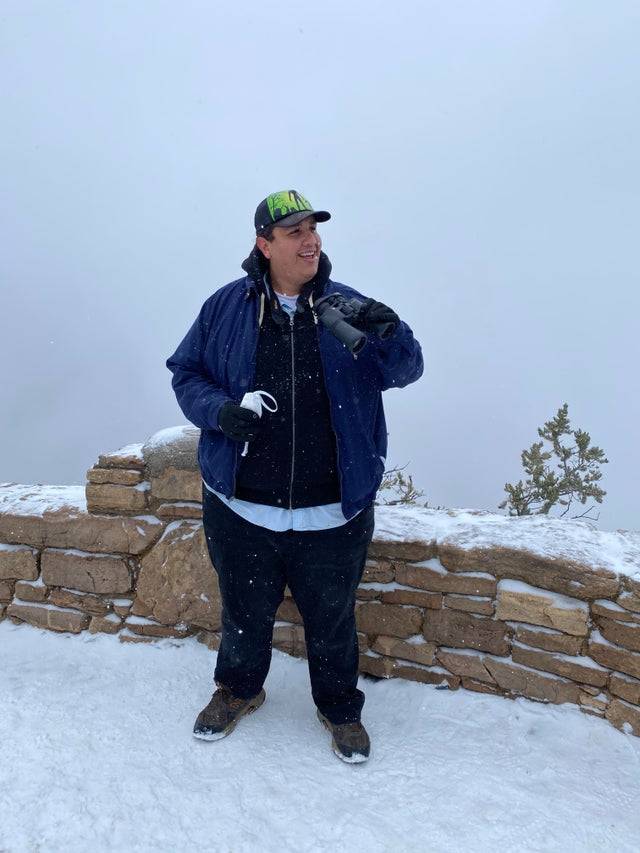 A man smiling holding binoculars in front of a very foggy background