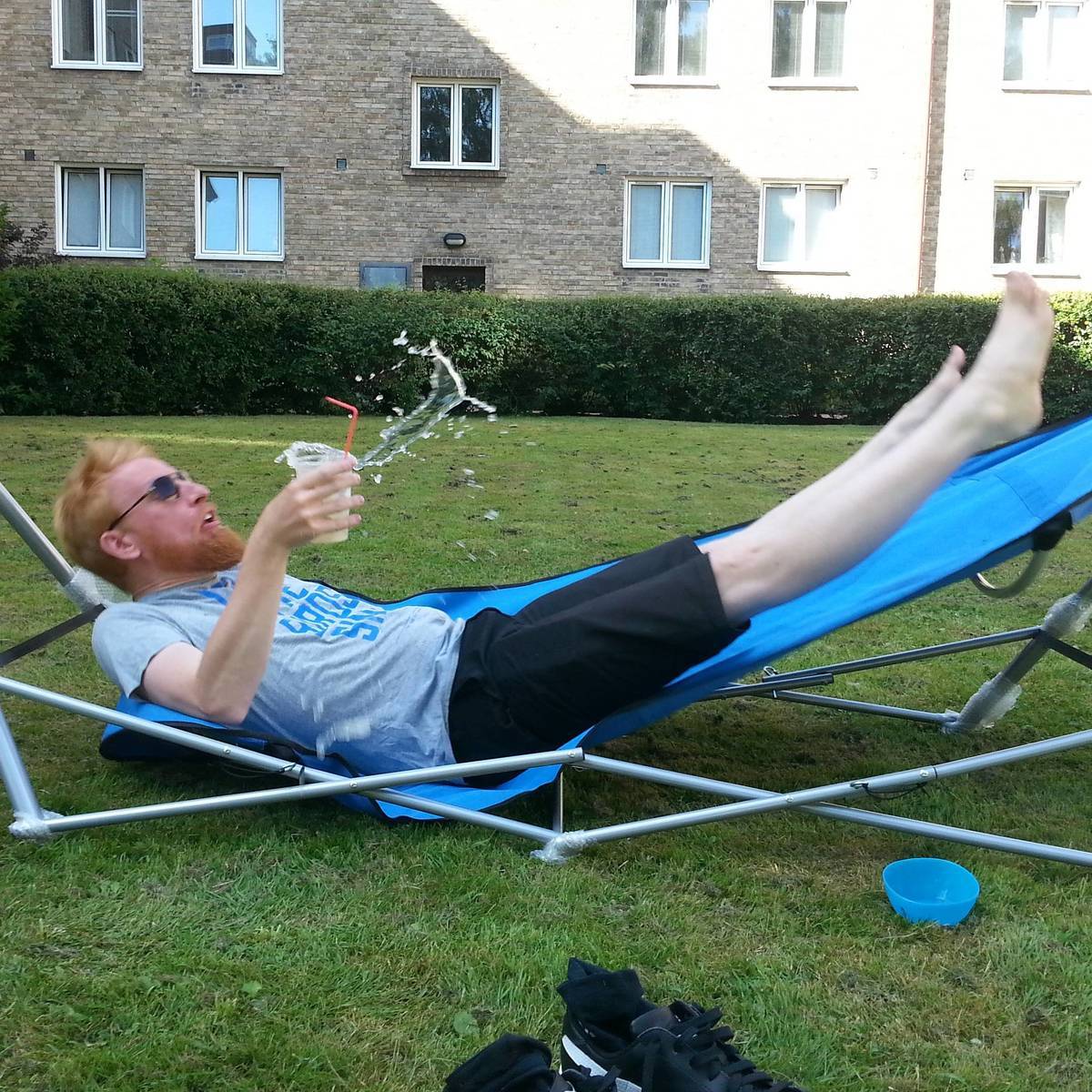 Man falling back on a hammock with drink in his hand. 