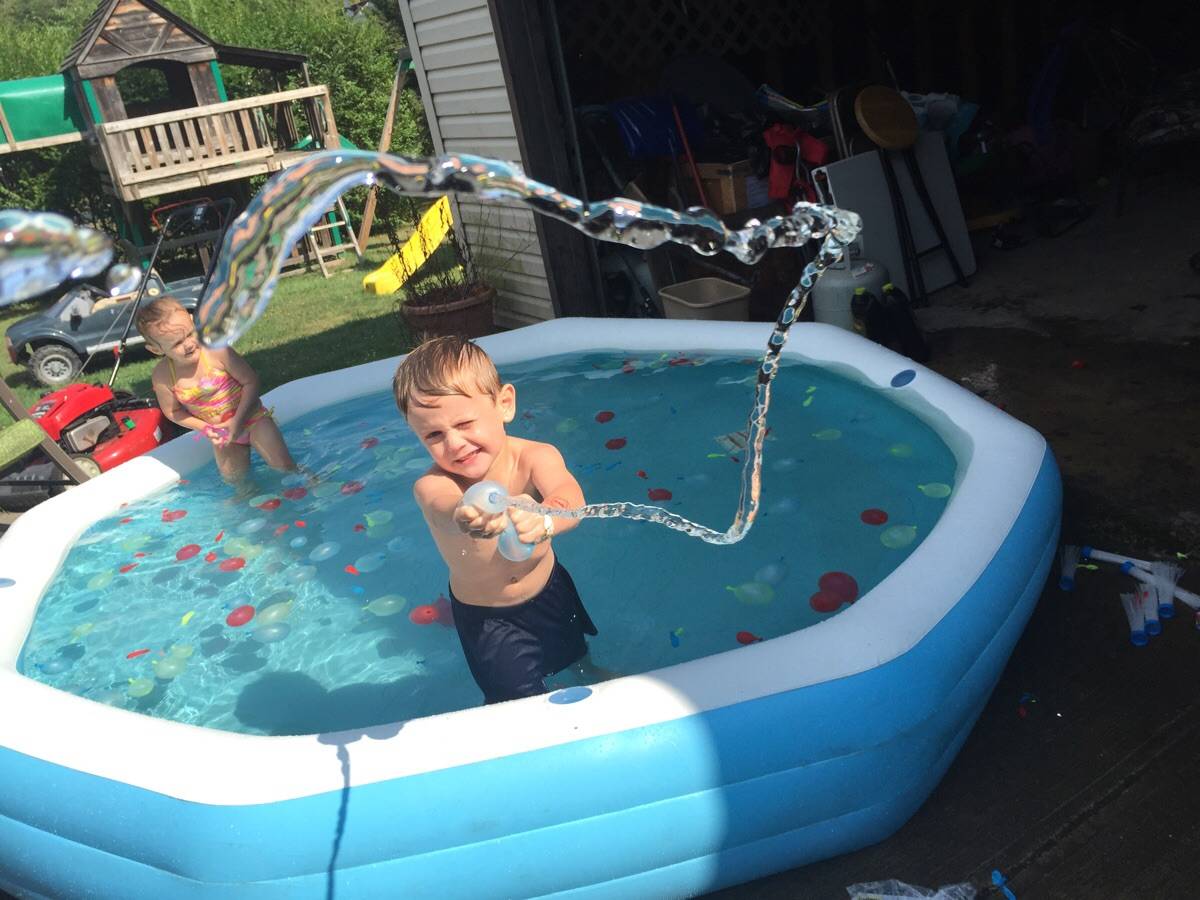 Two kids in an inflatable pool. Water gun being shot at the camera. 