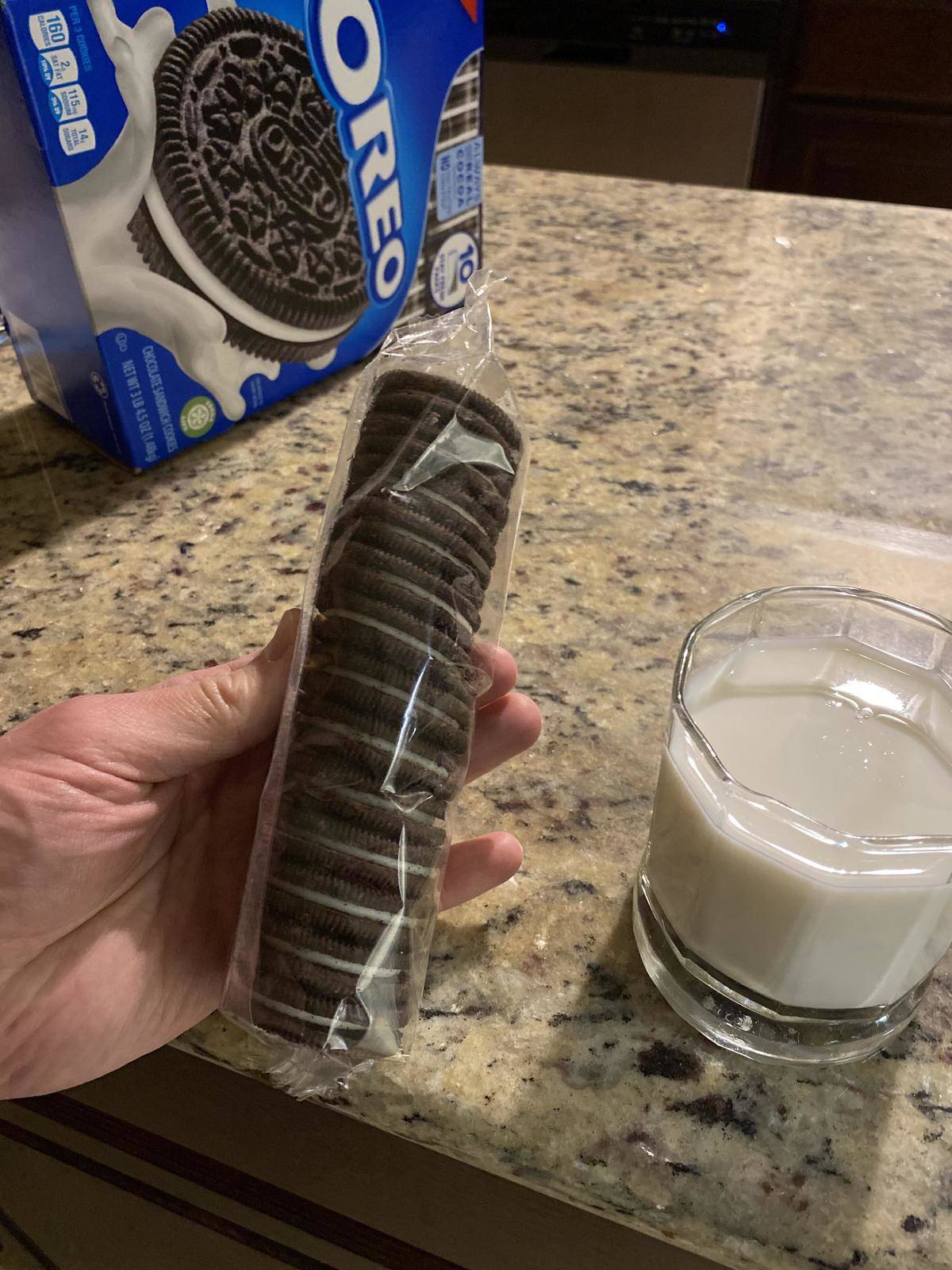 Oreo cookies conveniently packaged in individual sleeves being held out beside a glass of milk