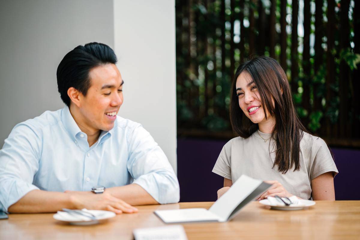 Couple chatting, woman laughing sitting at table with book open in front of her