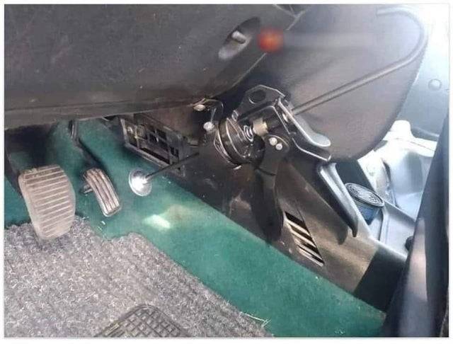 Caulking gun attached under the steering wheel of a car.  