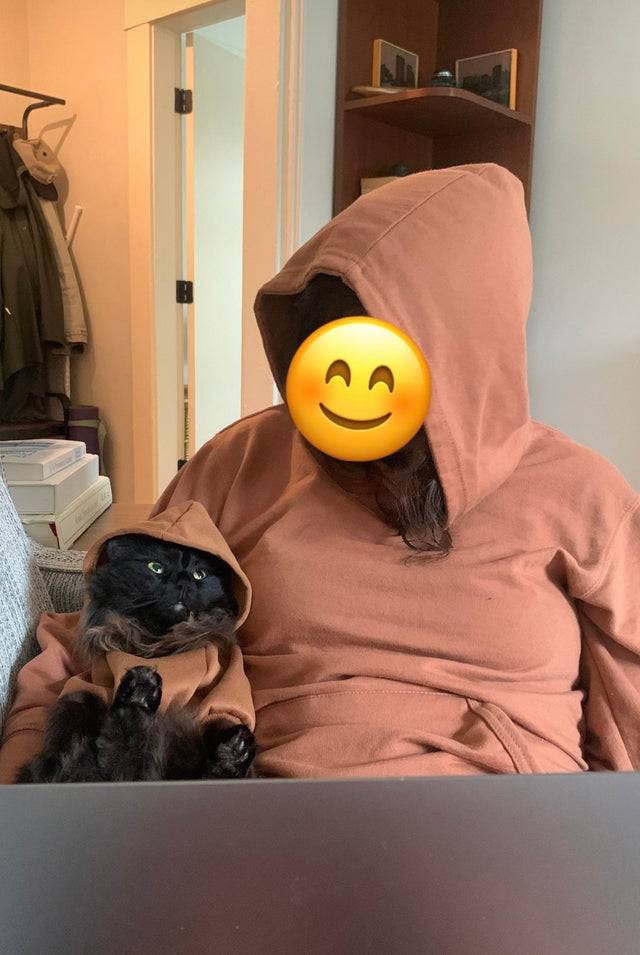 Woman and her cat wear identical salmon-colored hoodies. 