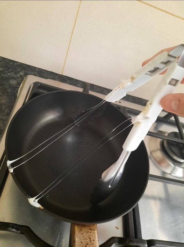 Plastic tongs melting overtop of a frying pan. 