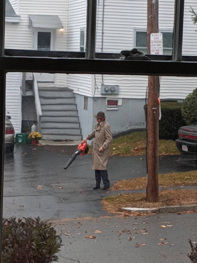 The person holding a leaf blower wearing a brown trench coat