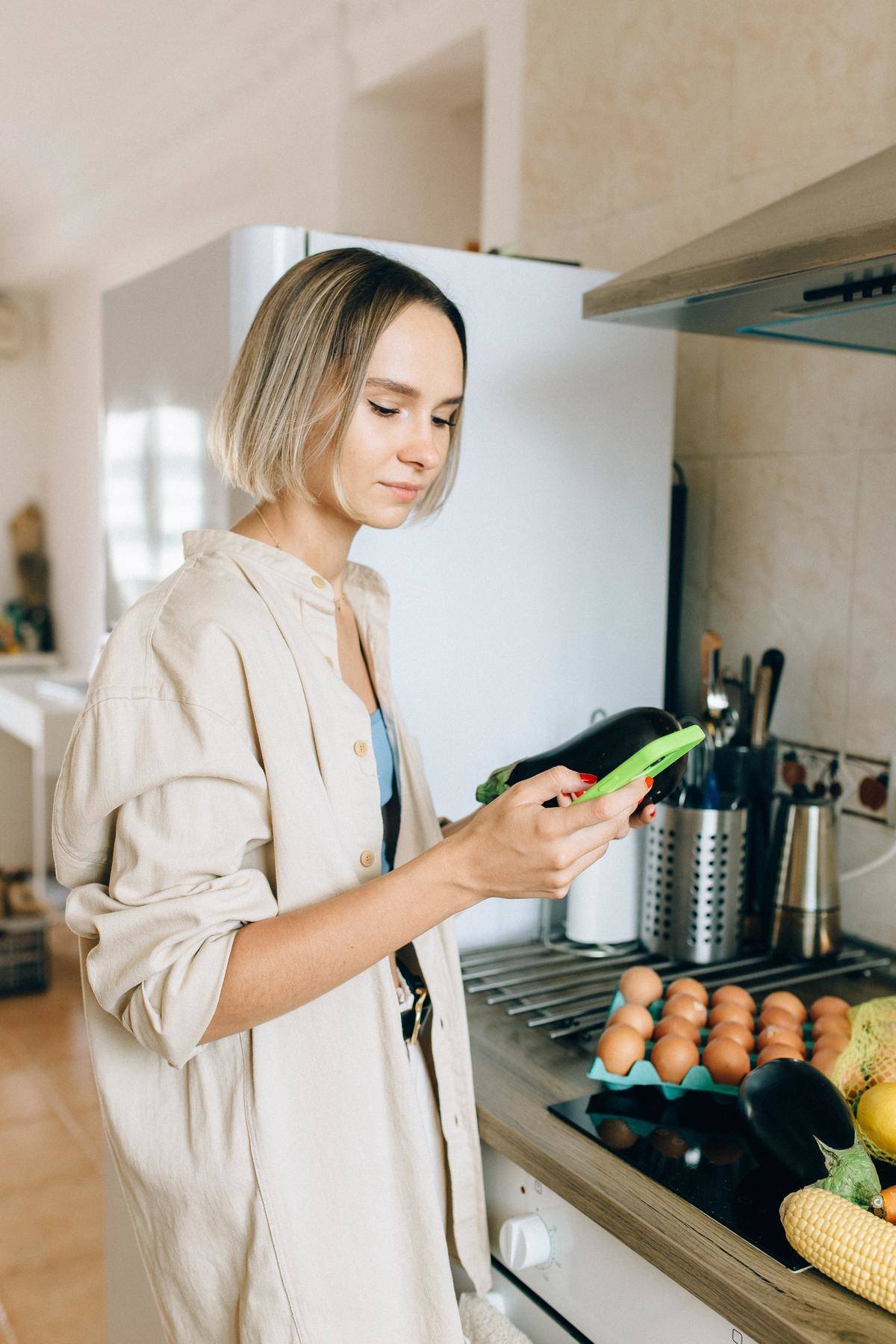 blonde woman in beige shirt checking cell phone while standing in kitchen