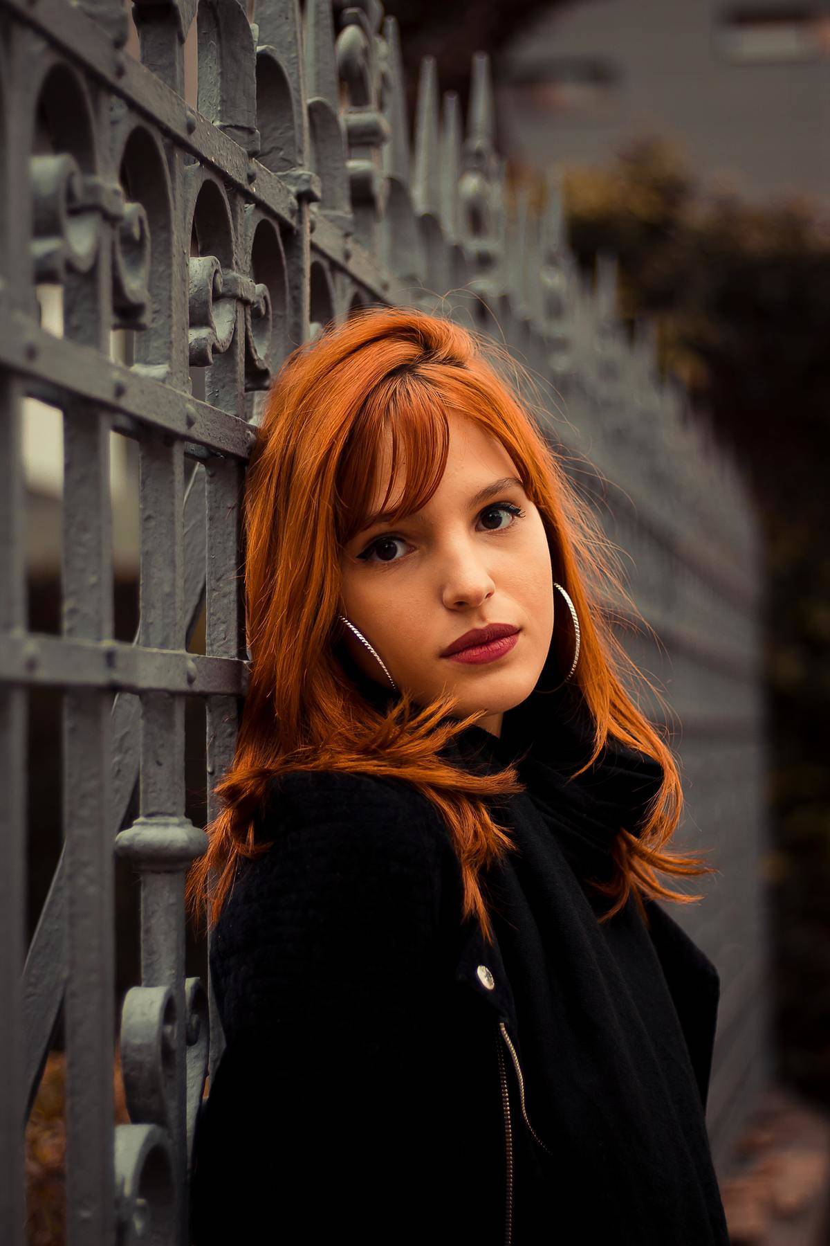 Redheaded woman leaned against wrought iron fence