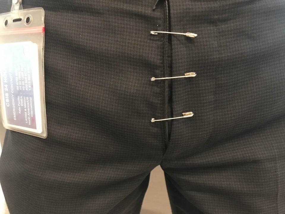 Three safety pins keeping together a man's pants where the fly zipper broke