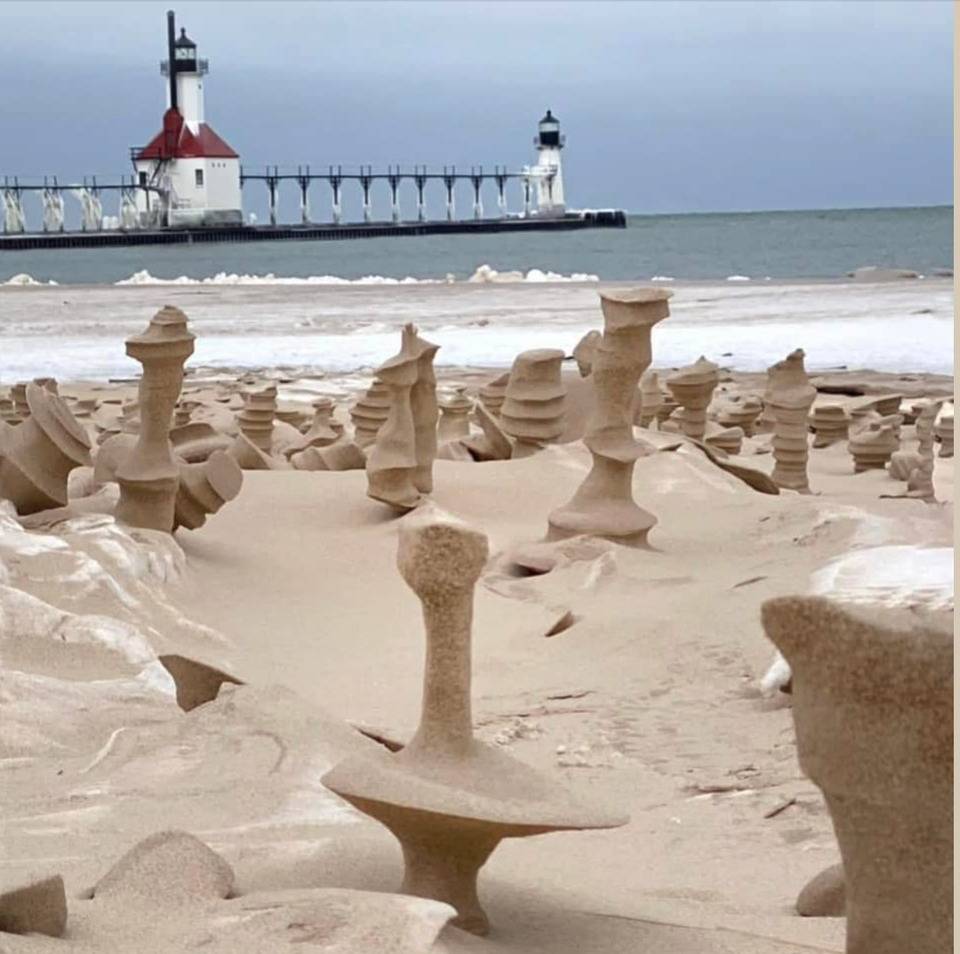 Sand formations on a beach with lighthouse in the background.