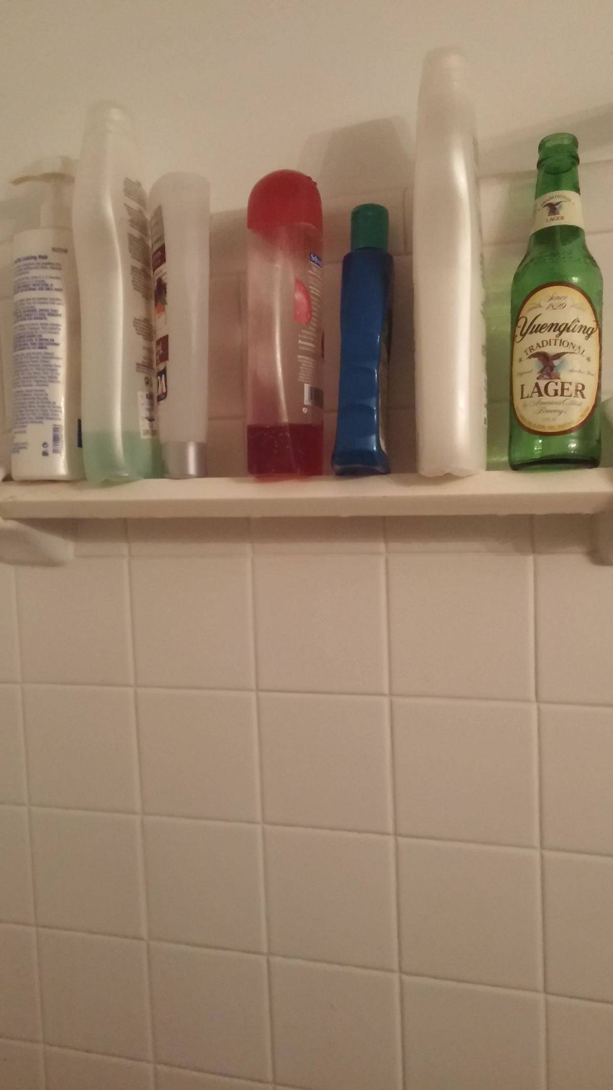 Shampoo bottles in shower next to empty beer bottle