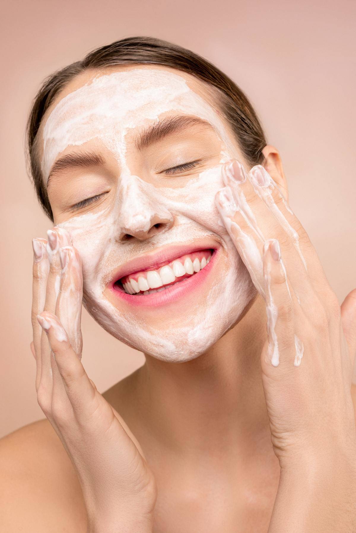 A woman smiles as she washes her face with a cleanser.