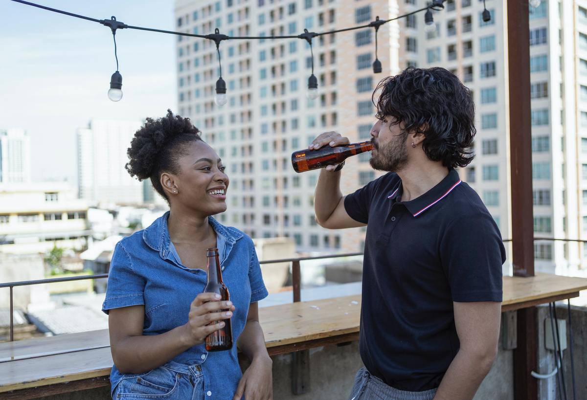 Couple talking on rooftop, each holding a beer bottle