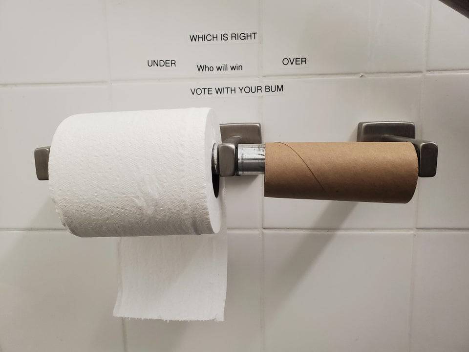 Text on the wall asking for people to vote on which toilet paper roll is better.