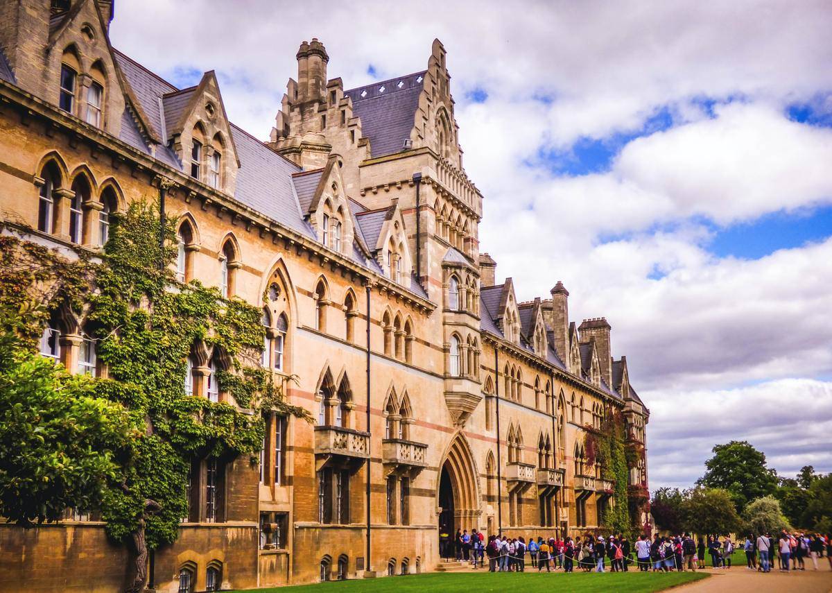 The exterior of a university with students waiting outside.