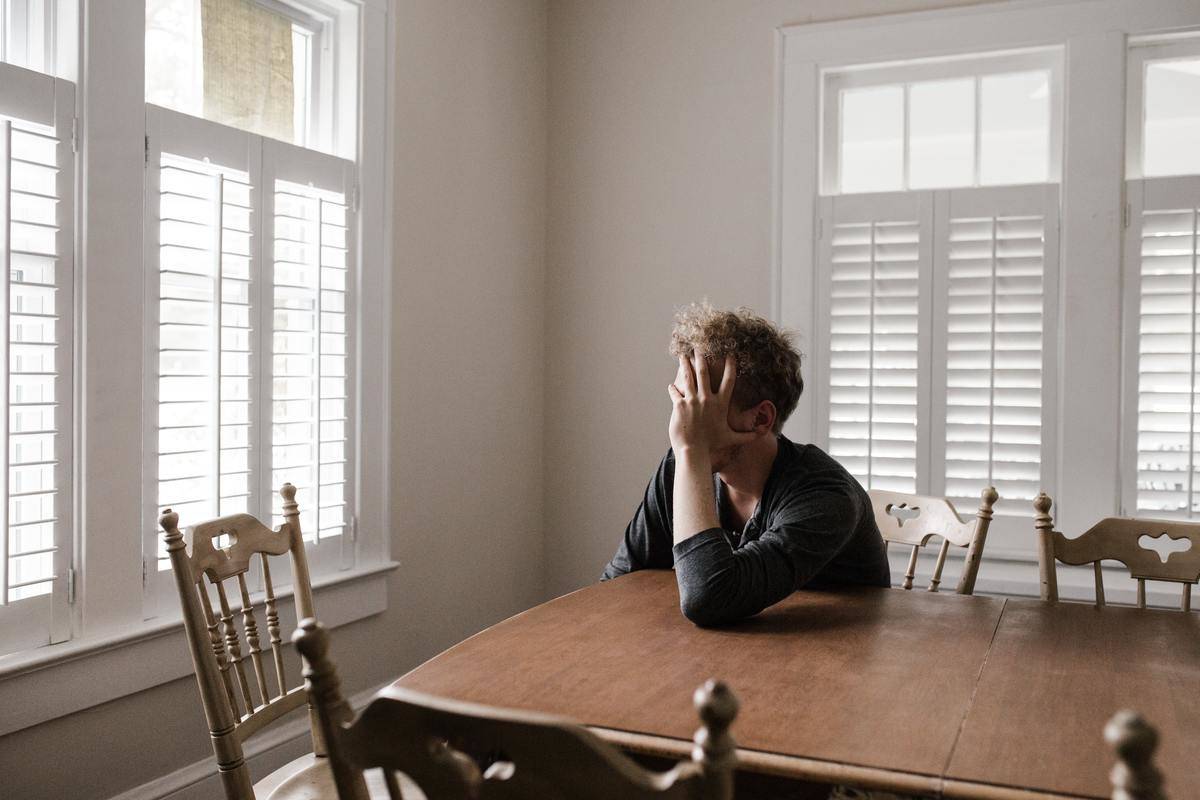 Man sits at kitchen table with head in his hands.