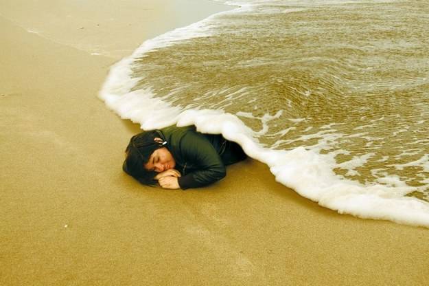 Woman lying on beach and wave coming overtop of her.