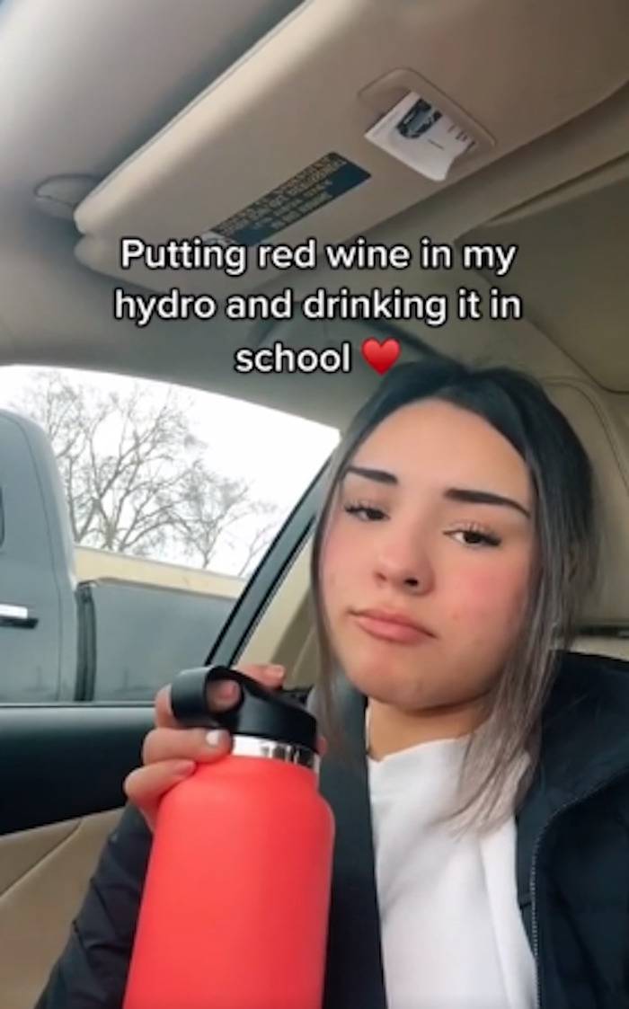 Woman drinks red wine in her water bottle in the car as she heads to school.