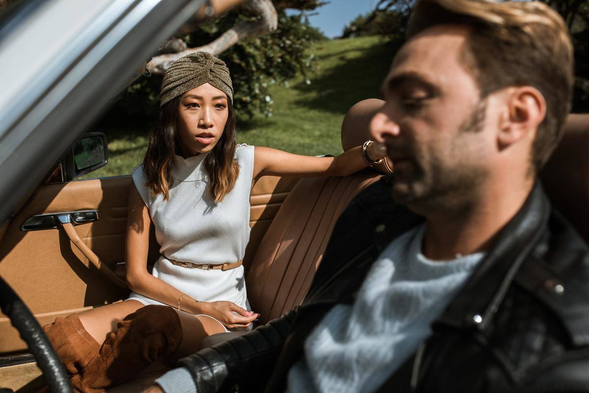 Couple in convertible car; woman is turned to look at man with an upset expression on her face
