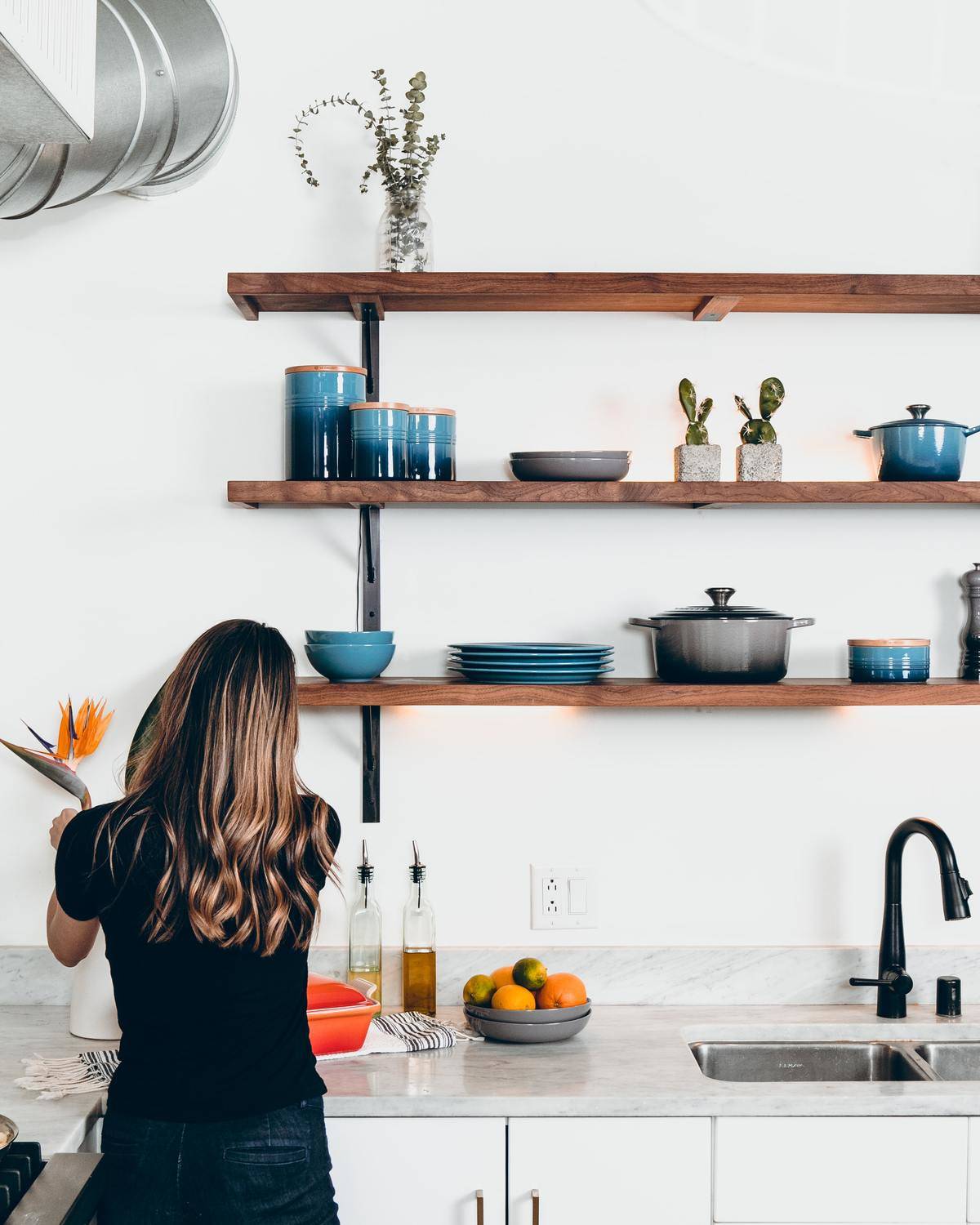 A woman works in a kitchen and has her back facing the camera.