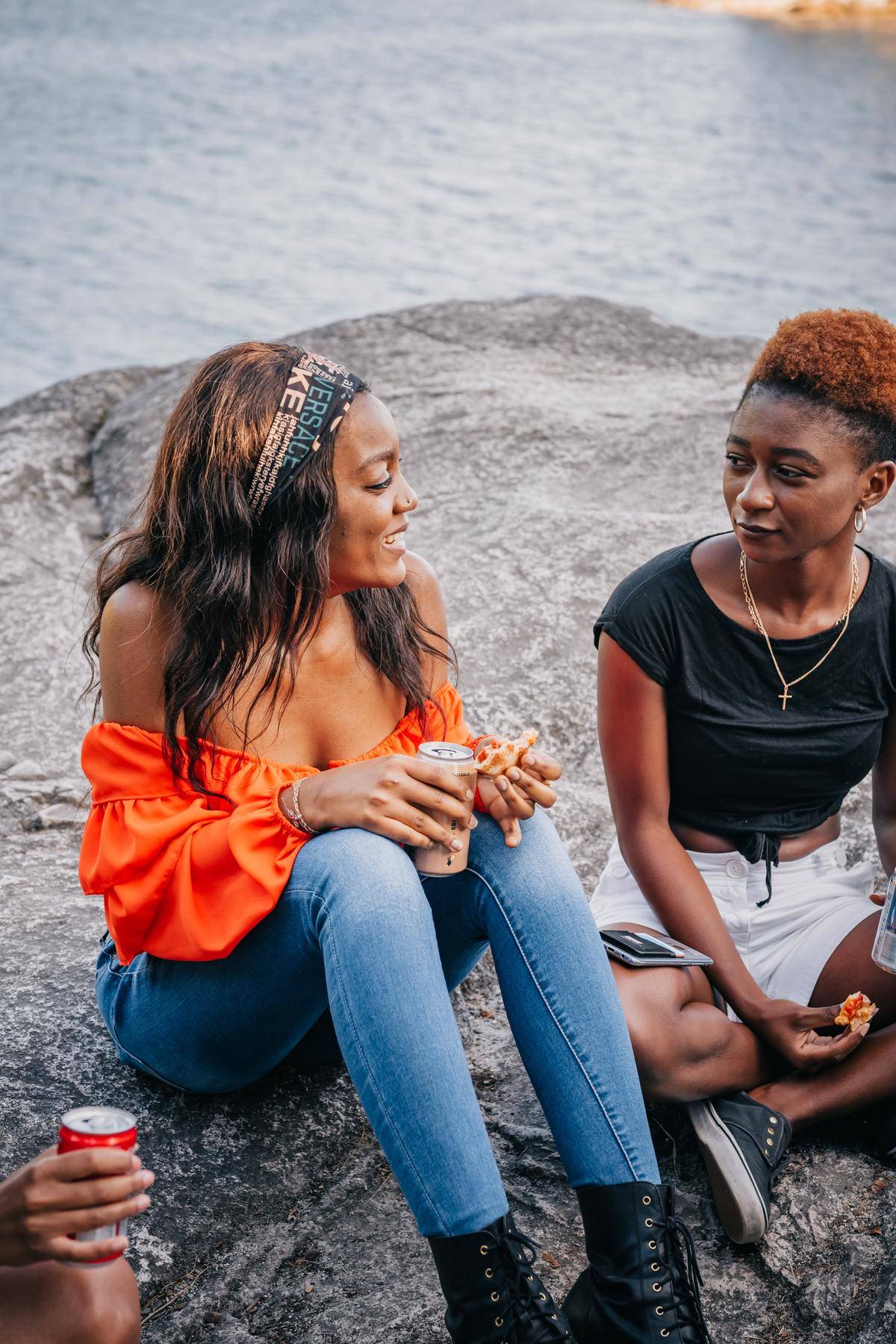 Two women sit outside near water talking