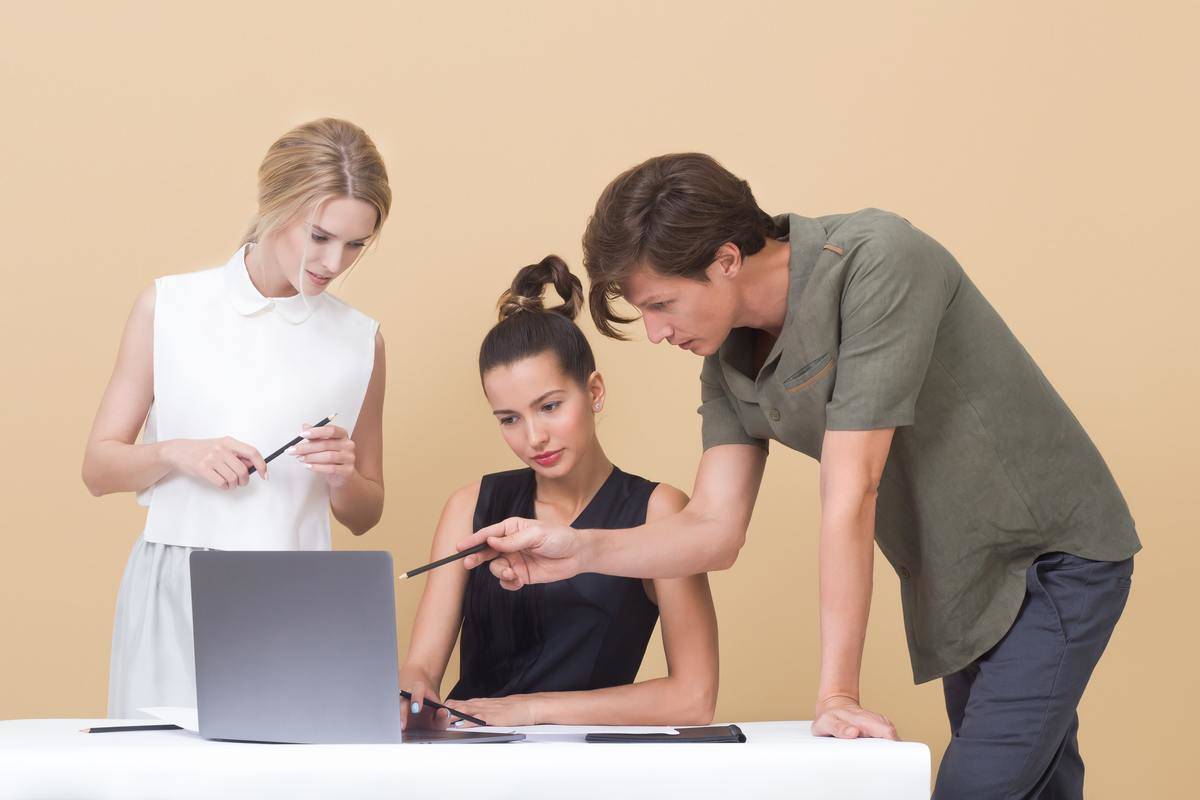 A man points at a laptop as two women look on.