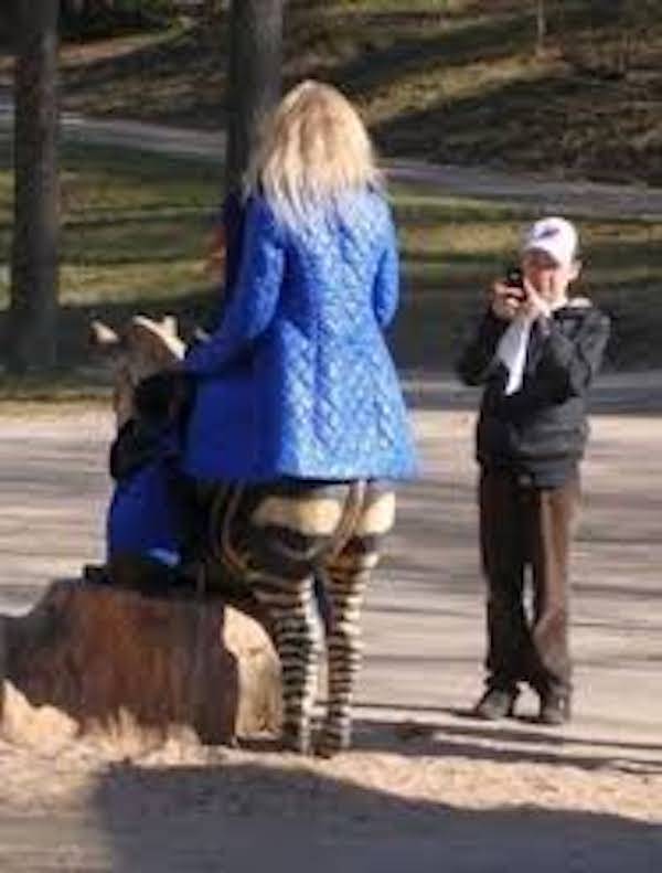 Woman riding rocking horse on a playground and child taking picture.