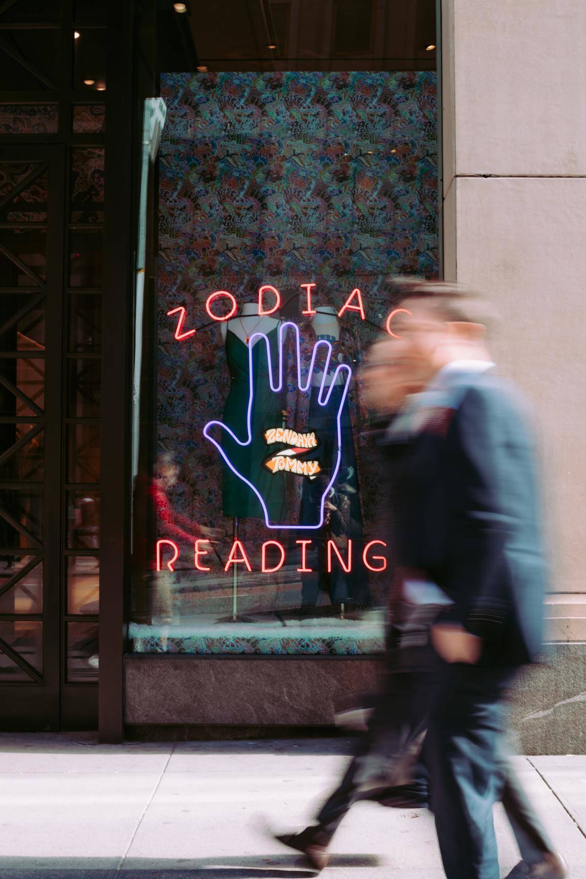 People walking down street blurry in front of zodiac reading store front