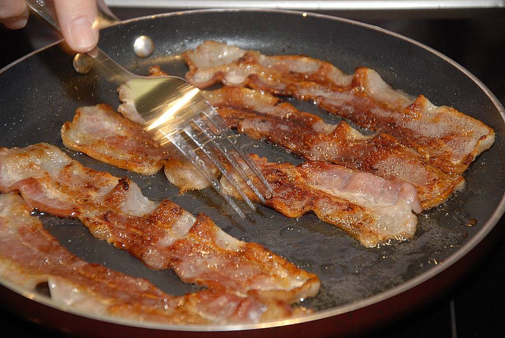someone using a fork to turn over bacon cooking in a pan
