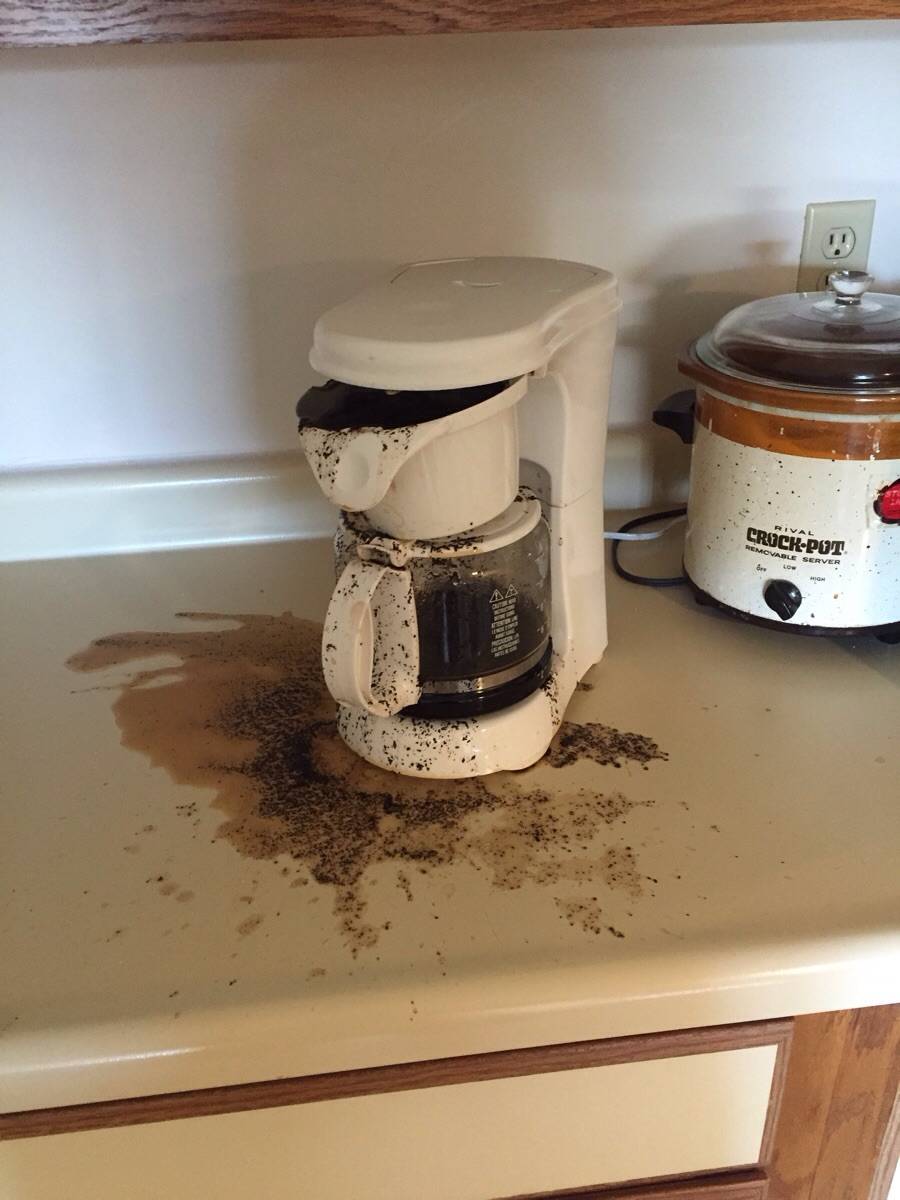 Coffee maker sitting on counter that is overflowing with coffee grounds
