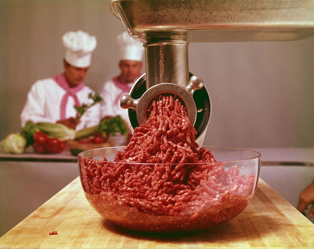 Close-up of uncooked ground beef in a glass bowl under a meat grinder