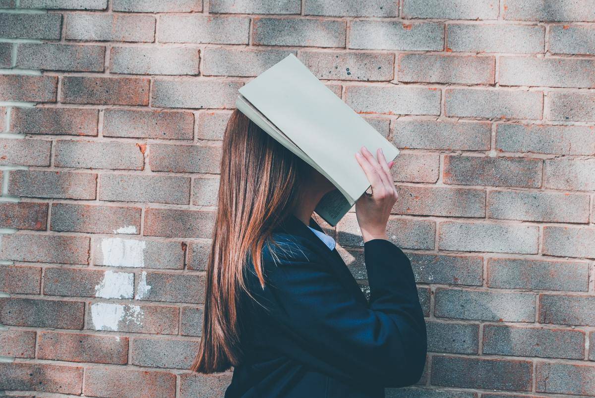 A frustrated high school student holds a book over her face.