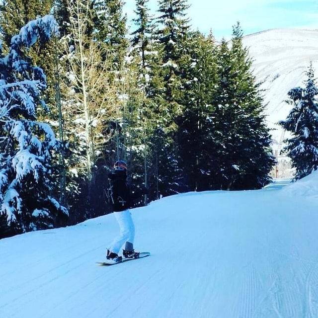 Person snowboarding down hill matching the snow and tree line