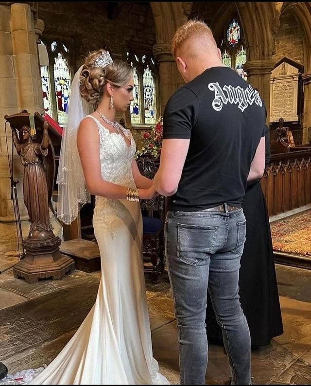 Bride and groom at the altar; she's wearing a wedding dress and full hair and makeup while groom is wearing jeans and a t-shirt.