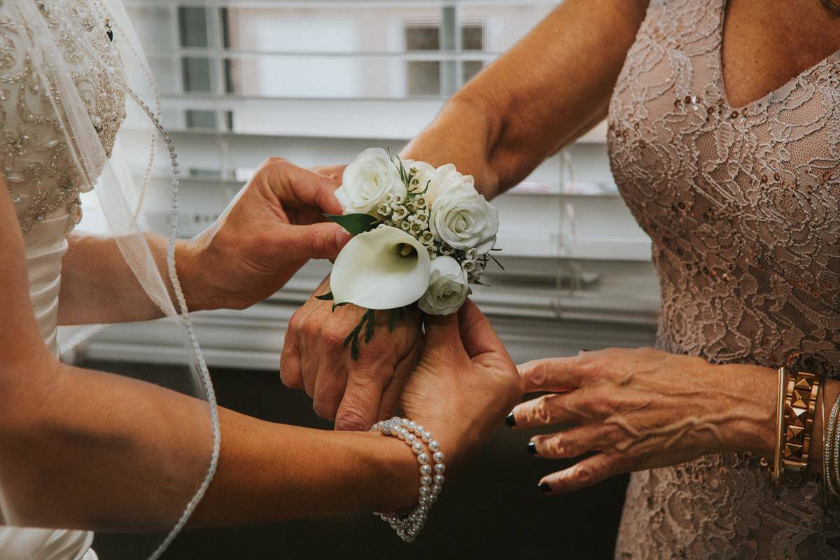 A bride puts a corsage on her mother's wrist.