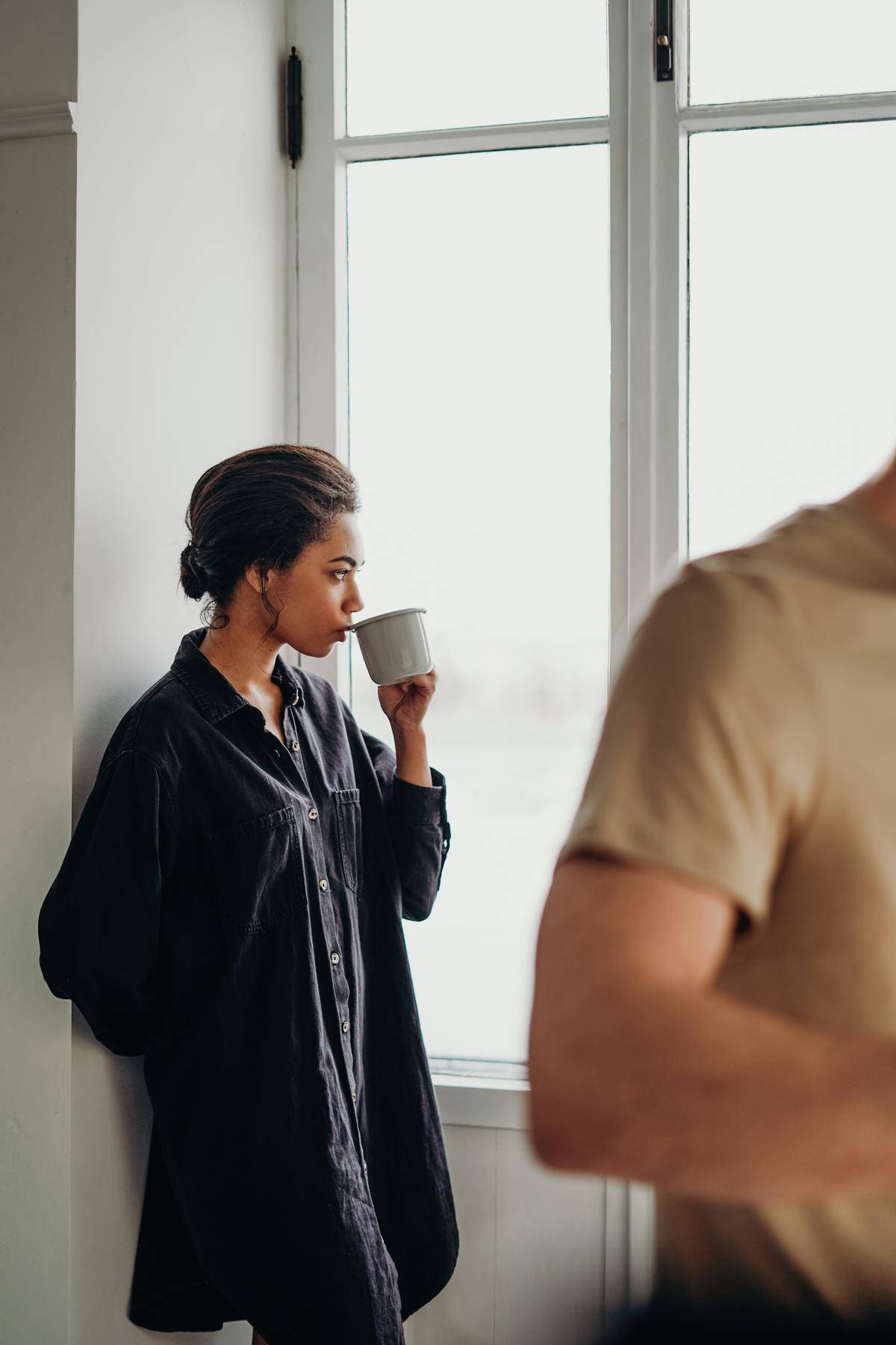 Woman sipping coffee looking out window thinking 