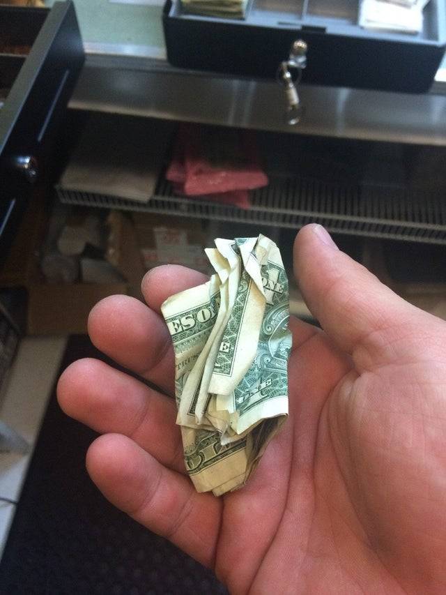 A person holds a crumpled one dollar bill.