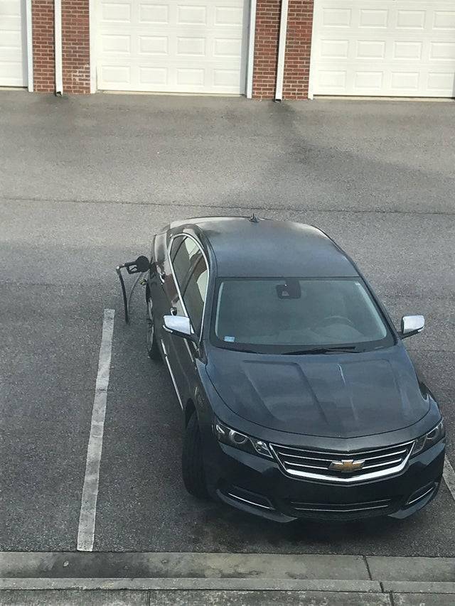 The nozzle from a gas station is stuck inside a car which is now parked in a parking lot. 