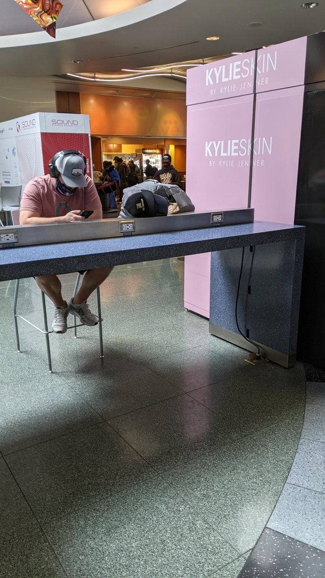 Man sitting at charging station on his phone with his backpack beside him creating optical illusion