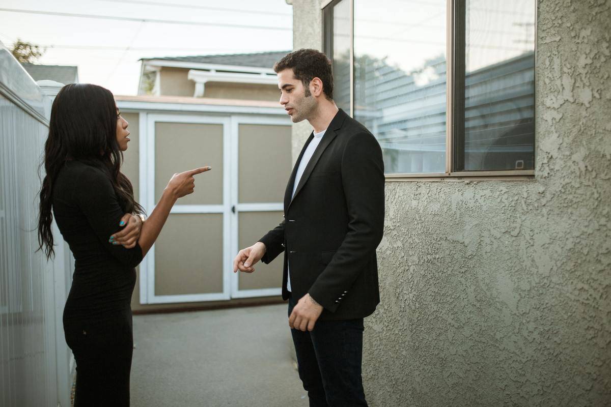 Woman points finger at man, they both wear black and stand outside