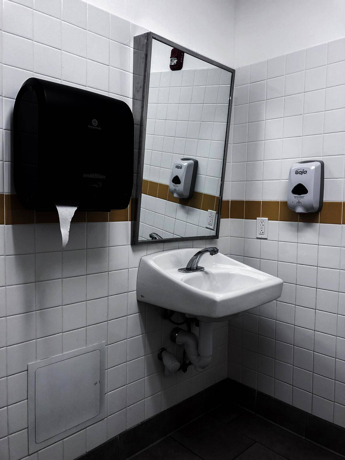 A sink, mirror, and soap/paper towel dispenser in a public bathroom.