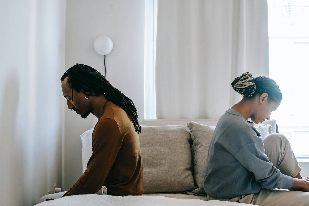 Man and a woman with their backs to each other sitting on bed