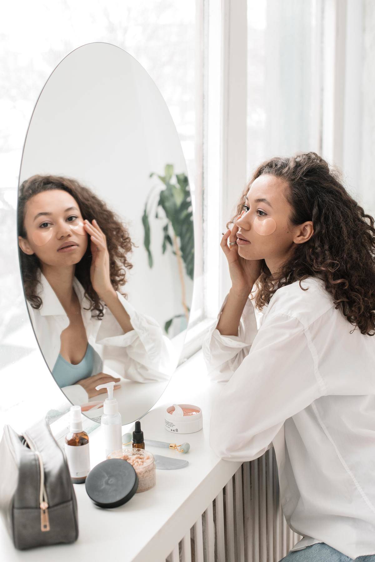 A woman looks into a mirror and does her skincare routine.