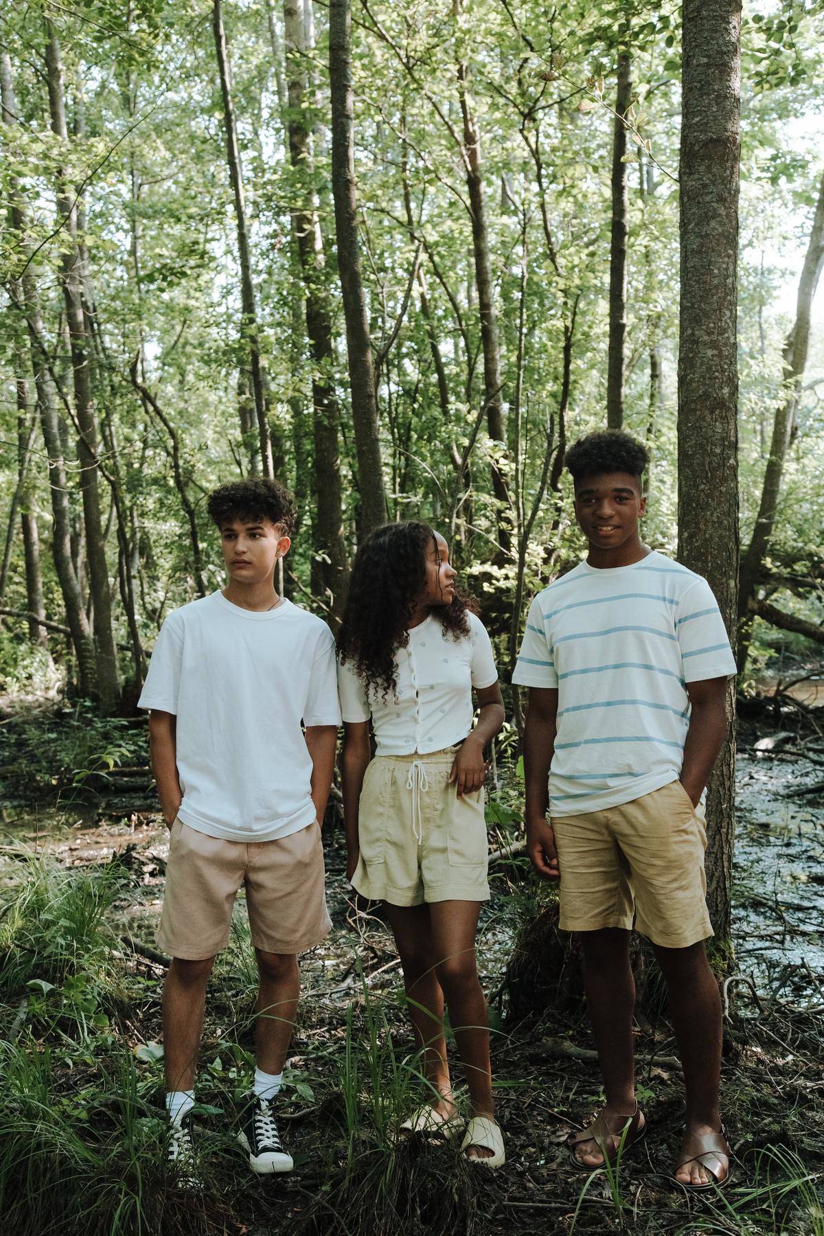 Three teenagers standing in forest.