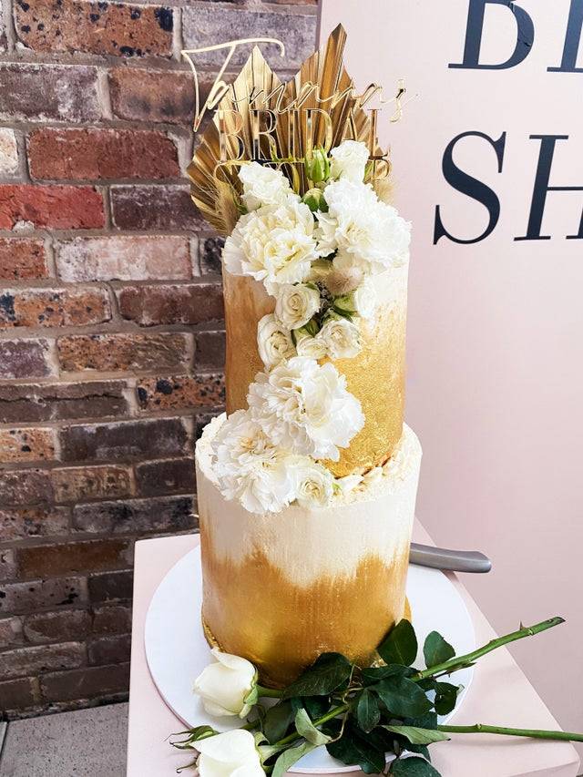 A gold and white tiered cake for a bridal shower.