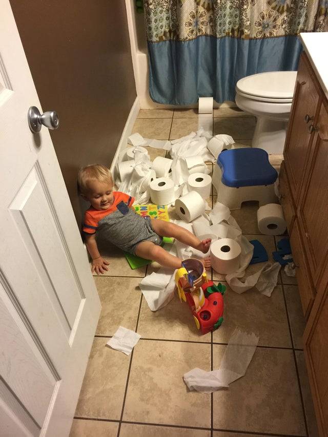Toddler laying among rolls of unspooled toilet paper in bathroom