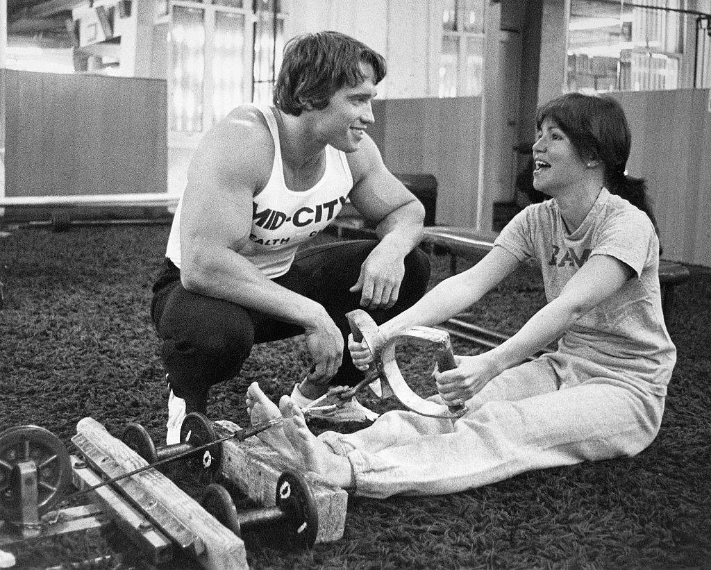 Actress Sally Field being trained by bodybuilder Arnold Schwarzenegger on the rowing machine
